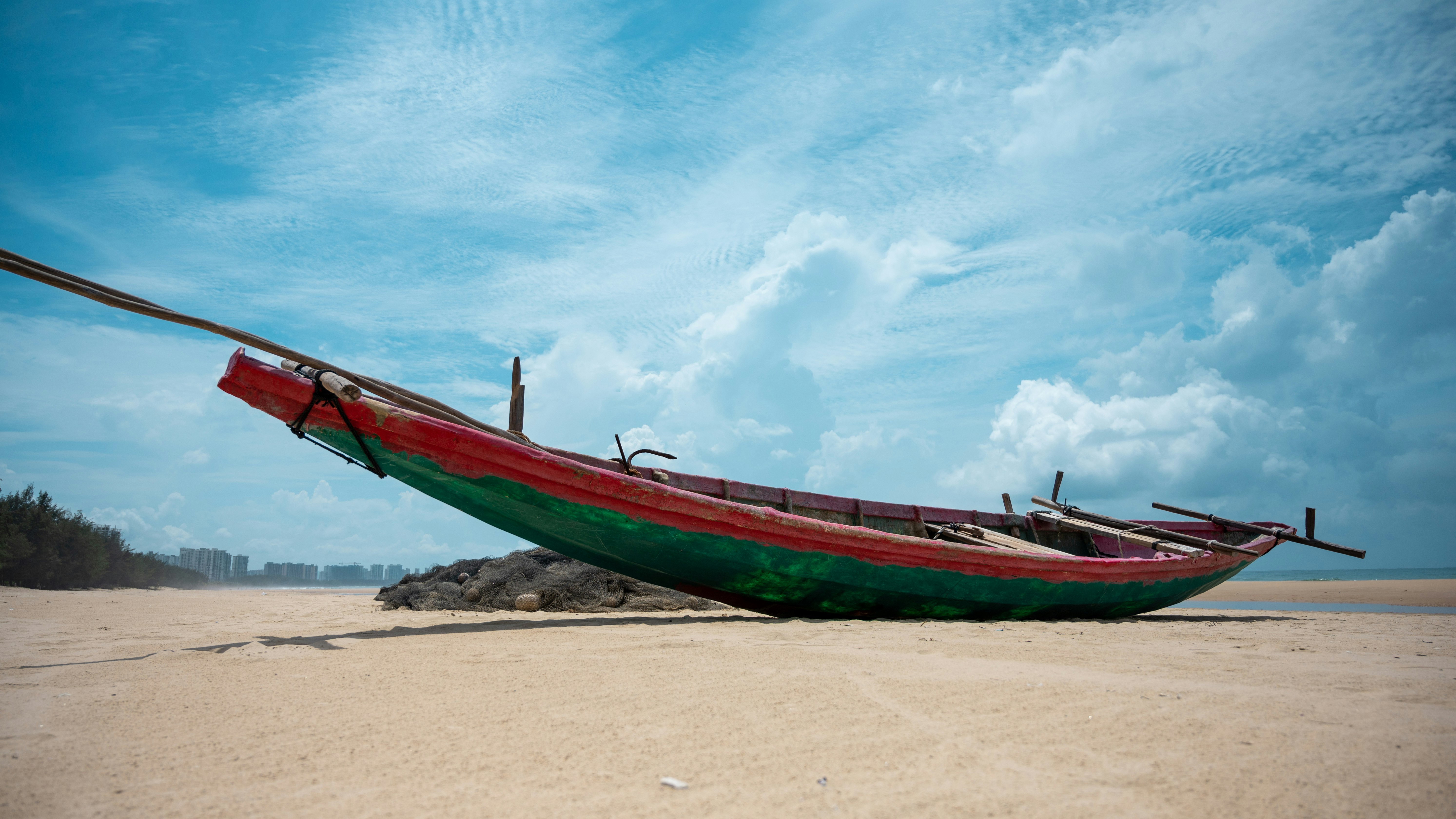 red and green boat on brown sand under blue sky during daytime